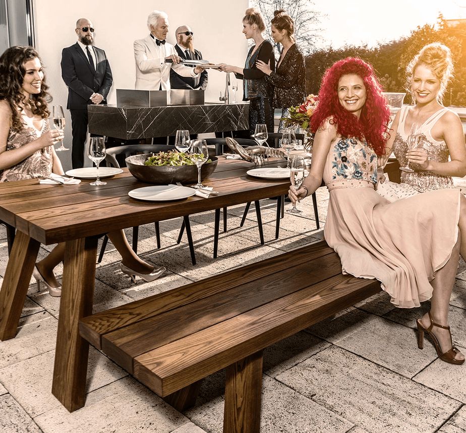 Vornehm gekleidete Gesellschaft auf einer Terrasse, die grillt und feiert.