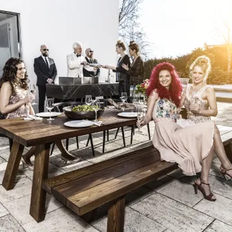 Vornehm gekleidete Gesellschaft auf einer Terrasse, die grillt und feiert.