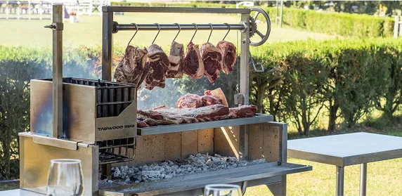 Tagwood Grill mit hängenden Fleischstücken und Kohlefeuer im Garten.