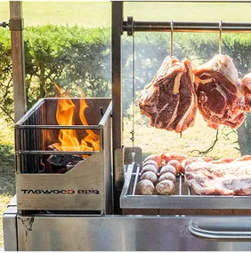 Fleisch und Würste auf einem Tagwood Grill mit brennendem Feuer, aufgehängt an Metallspießen.