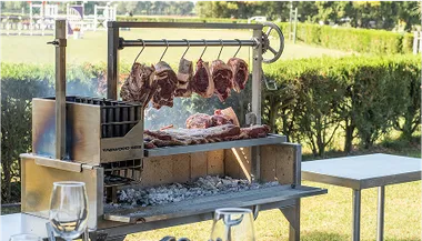 Tagwood Grill mit hängenden Fleischstücken und Kohlefeuer im Garten.